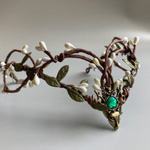 Brown branching tiara with pale buds, green leaves and a bright green round accent in its deer-head centrepiece.