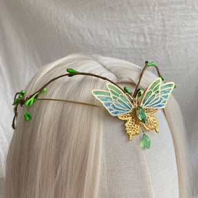 Close view of green-blue butterfly wings outlined in gold tone, with a green centre accent and drop on a delicate leafy band.