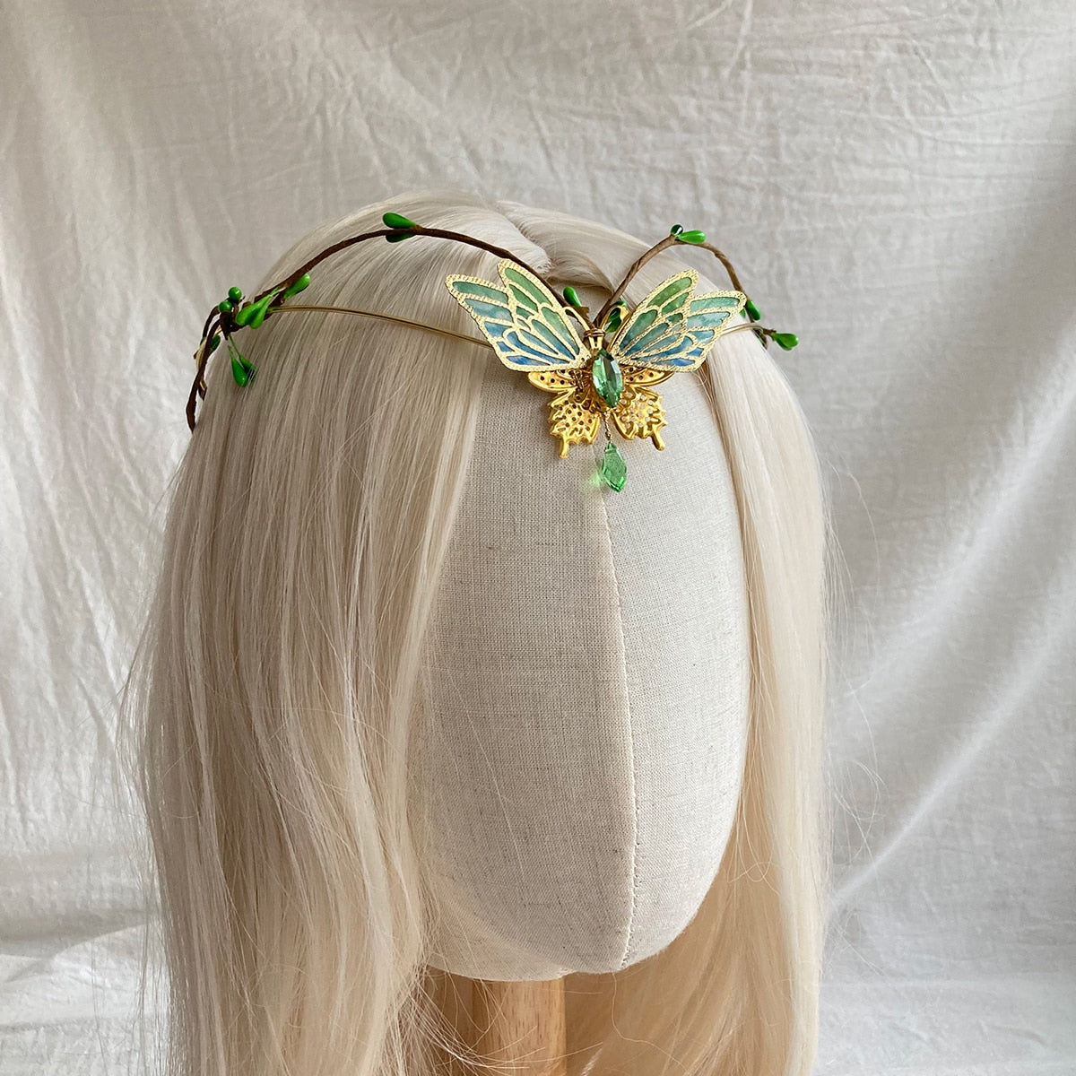 A delicate green butterfly tiara displayed across a pale-haired mannequin, showing the narrow leafy band and openwork wings.