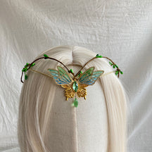 Gold-tone butterfly tiara with green-blue openwork wings, tiny green buds and a green hanging drop on pale hair.