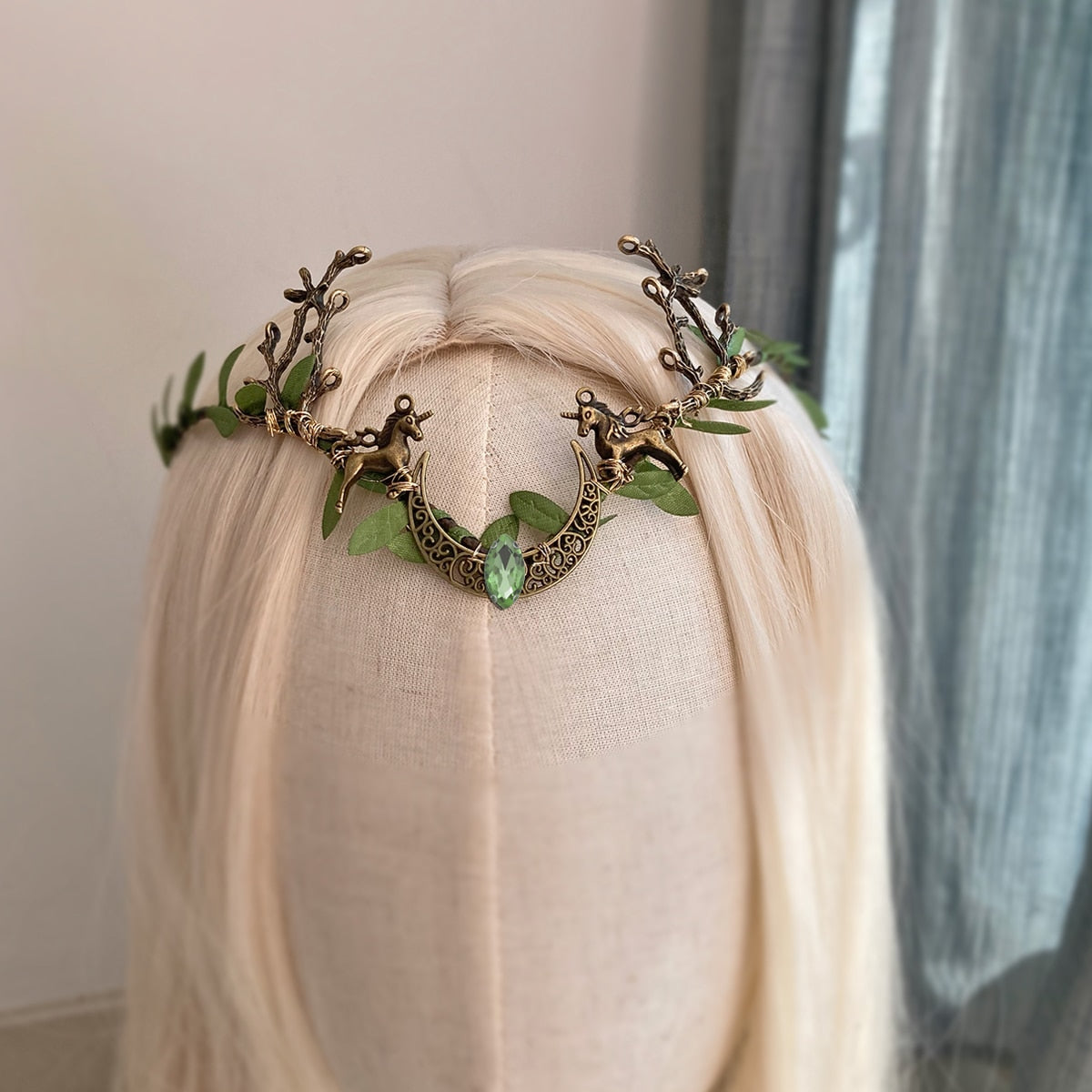 Leafy crescent-and-antler headpiece with a pale green central accent, displayed at an angle on a pale-haired mannequin.