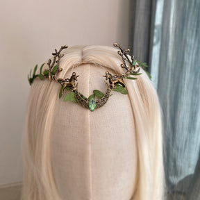 Leafy crescent-and-antler headpiece with a pale green central accent, displayed at an angle on a pale-haired mannequin.