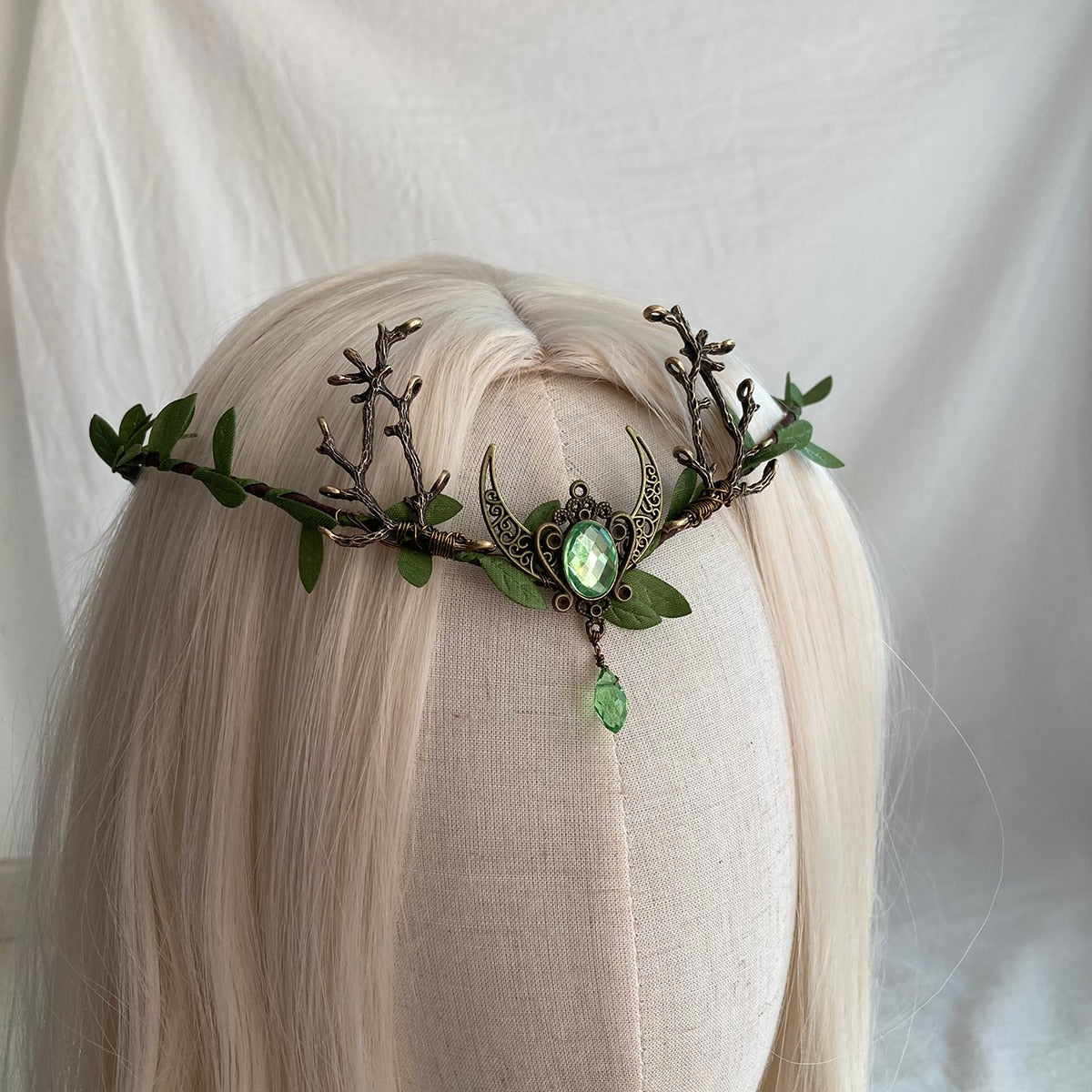 Green crescent-and-antler tiara on pale hair, with a bright oval centre and matching teardrop below the moon.