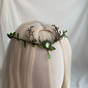 Green crescent-and-antler tiara on pale hair, with a bright oval centre and matching teardrop below the moon.