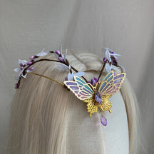 Gold-tone butterfly tiara with purple openwork wings, purple buds and a matching drop, displayed on pale hair.