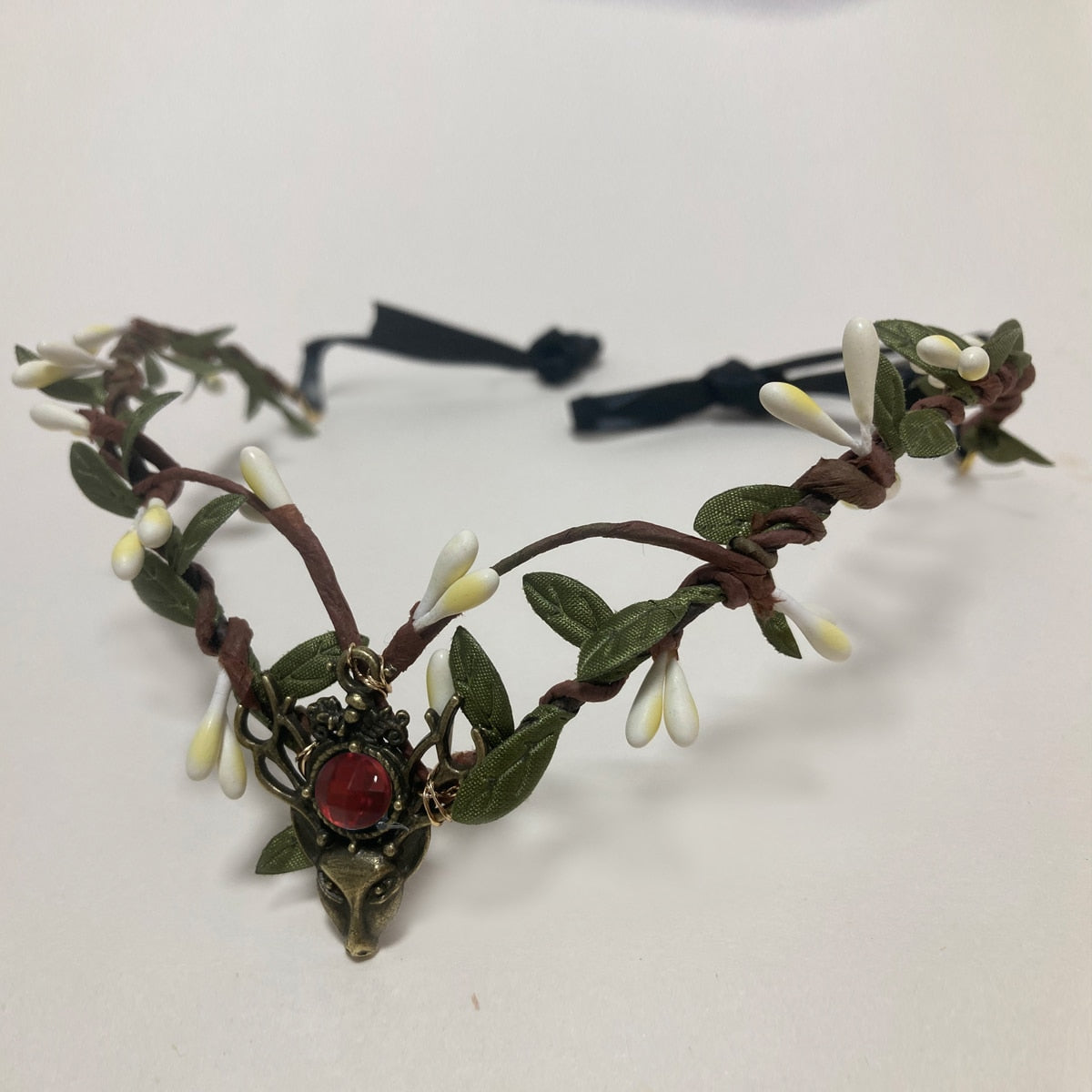 A dark red round accent decorates a deer-head centrepiece on a brown vine tiara with pale buds and green leaves.