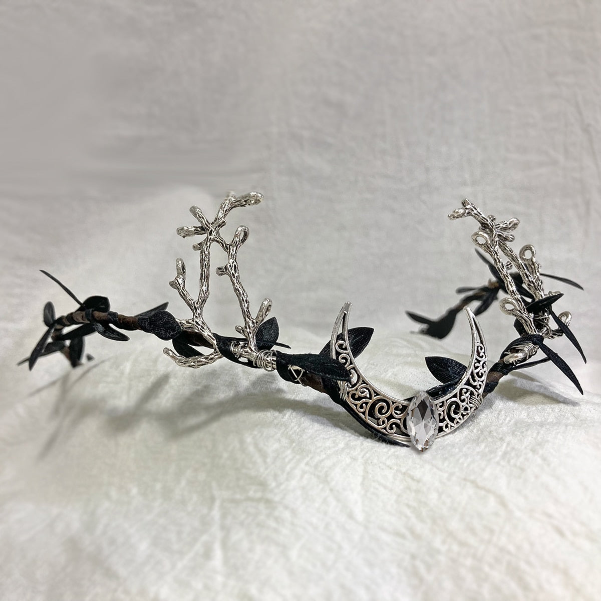 Silver-tone openwork crescent tiara with branching antlers, dark leaves and a clear drop at the centre.