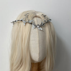 Silver-tone crescent and antler tiara on pale hair, with light leaf accents and a clear central drop.