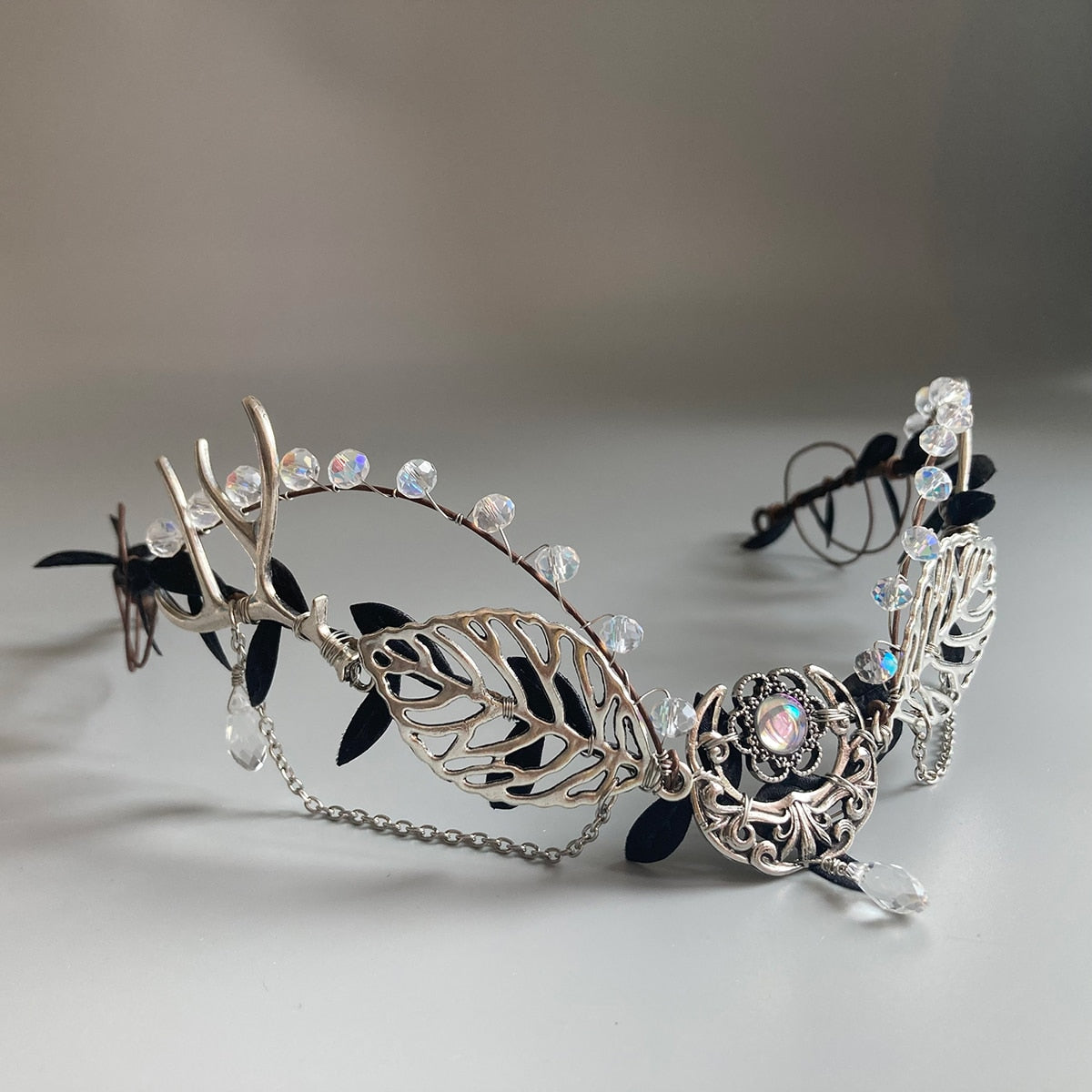 Angled side view of a silver-tone leaf crown showing clear beads along the upper edge, black foliage and fine draped chains.