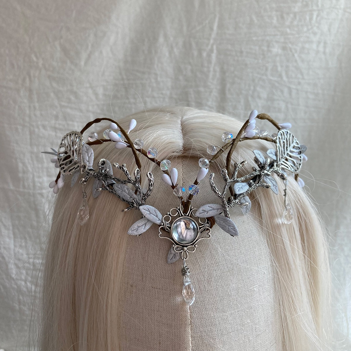 Silver-tone leaf headpiece with a round clear centre, small pale buds and a hanging teardrop, displayed on pale hair.