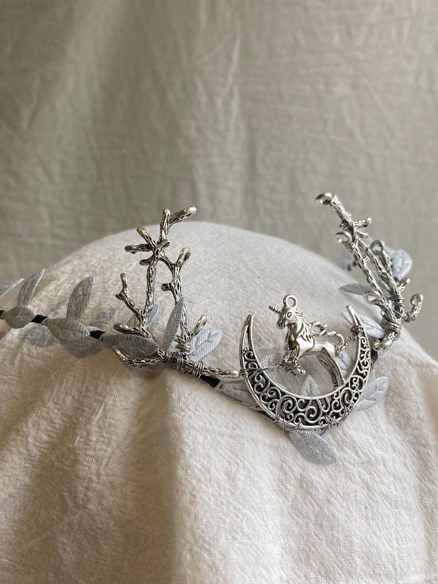 Silver-tone woodland tiara with branching antlers, pale leaves and a small unicorn above an openwork crescent.