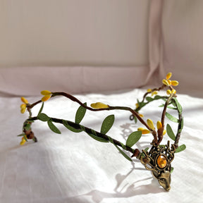Angled view of a brown vine tiara with yellow buds, green leaves and an amber-coloured deer-head centre.