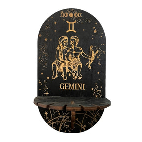 Black wall display shelf with gold-tone Gemini twins, zodiac symbol, stars and GEMINI lettering above a small ledge.