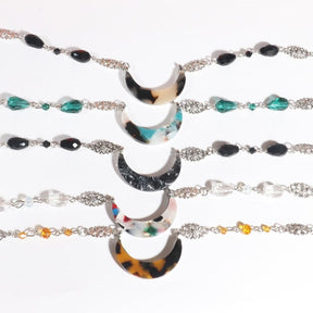 Five acrylic crescent headdresses arranged in rows, showing beige tortoiseshell, teal marble, black marble, colourful flecks and amber tortoiseshell designs with coordinating beads.