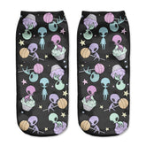Black alien socks with pastel aliens, flying saucers, planets and little stars, displayed as a matching pair on a pale background.