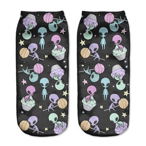 Black alien socks with pastel aliens, flying saucers, planets and little stars, displayed as a matching pair on a pale background.