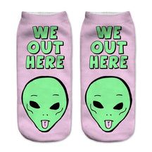 Pink socks with bold green We Out Here lettering above an alien head sticking out its tongue.