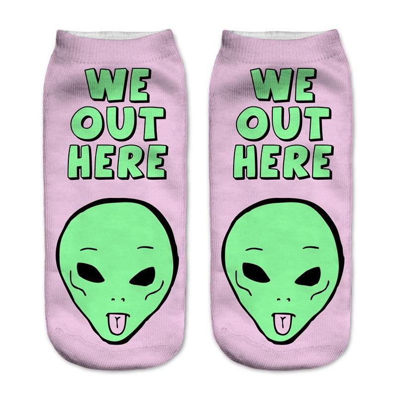 Pink socks with bold green We Out Here lettering above an alien head sticking out its tongue.