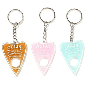 Amber, pale pink and aqua planchette keychains lined up on white, each with white lettering, a circular opening and a silver-tone keyring.
