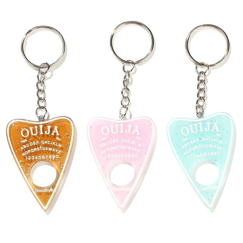 Amber, pale pink and aqua planchette keychains lined up on white, each with white lettering, a circular opening and a silver-tone keyring.