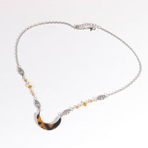 Silver-tone headdress with an amber-and-black tortoiseshell-style acrylic crescent and small amber beads, arranged in an oval on a pale background with the clasp and chain visible.