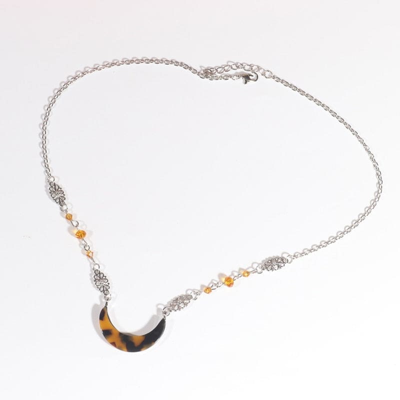 Silver-tone headdress with an amber-and-black tortoiseshell-style acrylic crescent and small amber beads, arranged in an oval on a pale background with the clasp and chain visible.