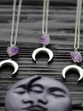 Amethyst crescent moon necklace in the Smooth Crescent design, arranged on dark wood with purple moon decor.