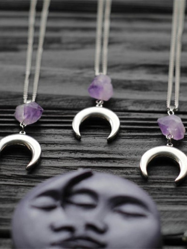 Amethyst crescent moon necklace in the Smooth Crescent design, arranged on dark wood with purple moon decor.