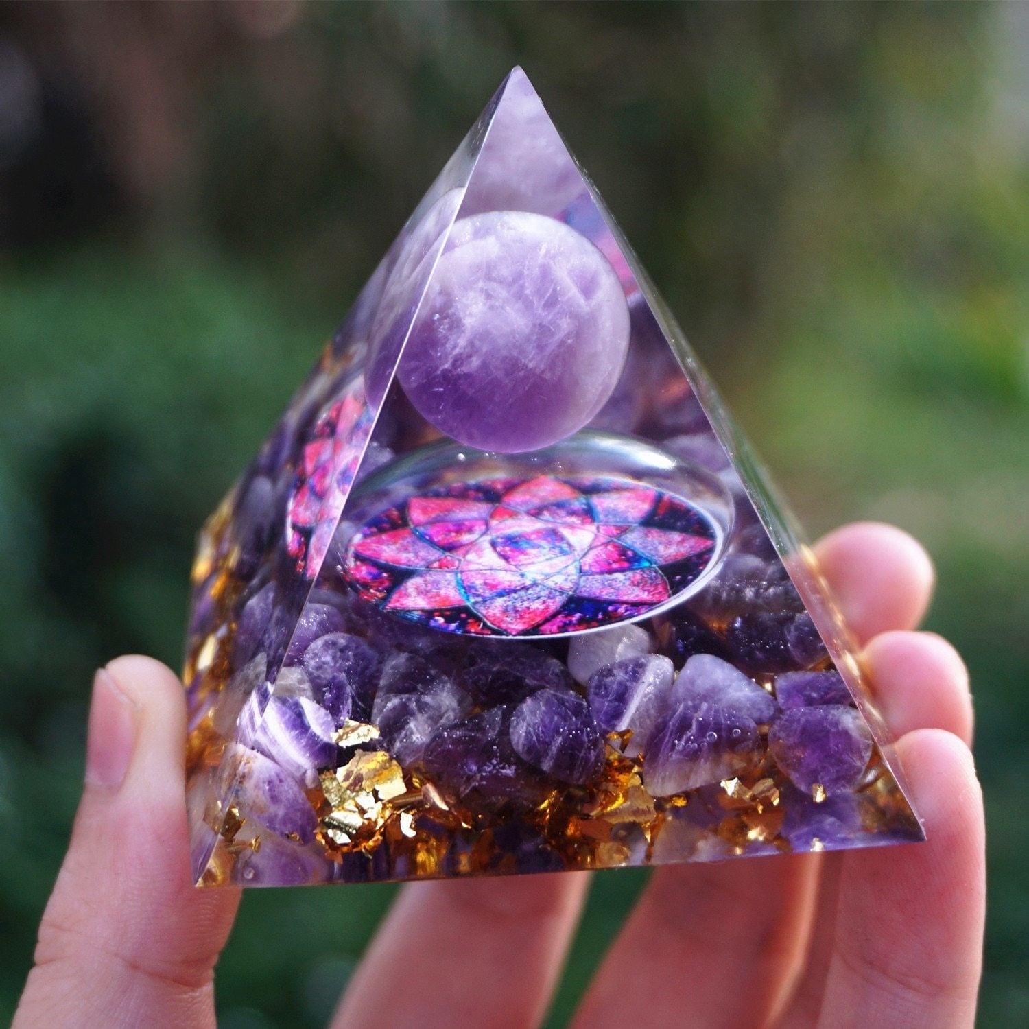 Close front view of an amethyst lotus orgone pyramid, with a purple sphere above a pink-purple lotus motif and amethyst-filled base.