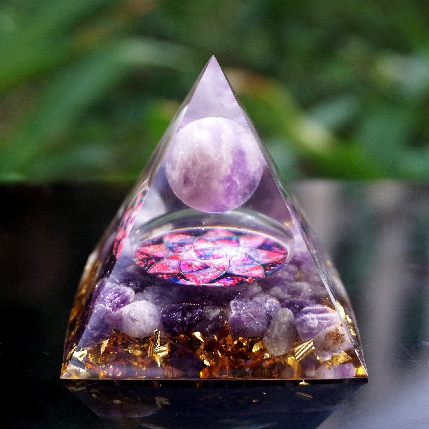 Amethyst lotus pyramid displayed upright on wood, with the pink-purple flower motif facing forward beneath the round stone.