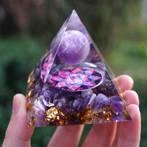 Amethyst lotus pyramid resting on an open hand, showing its complete outline and purple sphere above the flower motif.