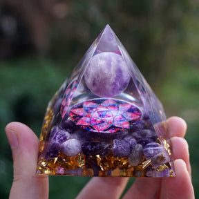 Low angled view of the clear lotus pyramid, with an amethyst sphere and purple stone pieces visible above the supporting hand.