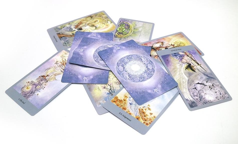 A scattered spread of fantasy tarot cards, with detailed figures, branches and varied pastel-toned scenes.
