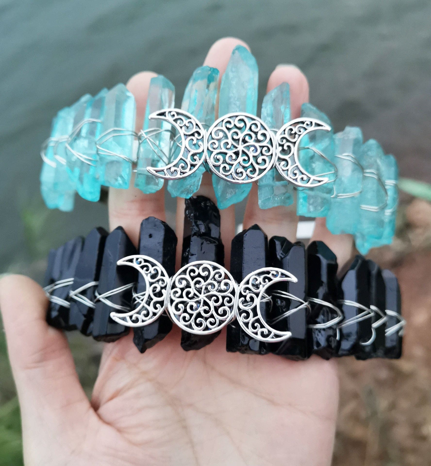 Aqua and black crystal point crowns shown together outdoors, with silver-tone triple moon emblems across the front.