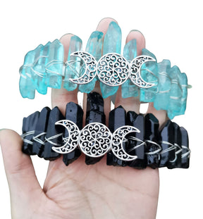 Aqua and black crystal crowns paired on white, showing matching silver-tone triple moon emblems and contrasting crystal points.