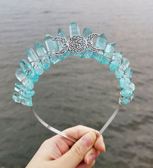 Front view of a aqua crystal point crown with a silver-tone triple moon emblem and wire-wrapped band.