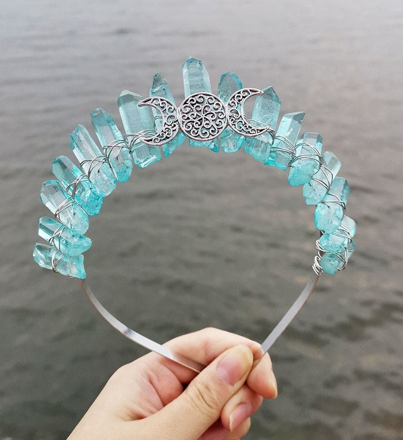 Front view of a aqua crystal point crown with a silver-tone triple moon emblem and wire-wrapped band.
