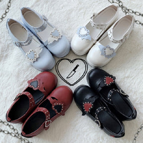 Four pairs of winged-heart Mary Janes in blue, white, red and black arranged on a white fluffy surface, showing their matching platform shapes.