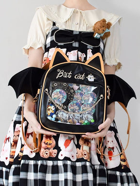 Bat cat backpack worn with a collared blouse and Halloween-print outfit, showing a collection of badges through the transparent front pocket.