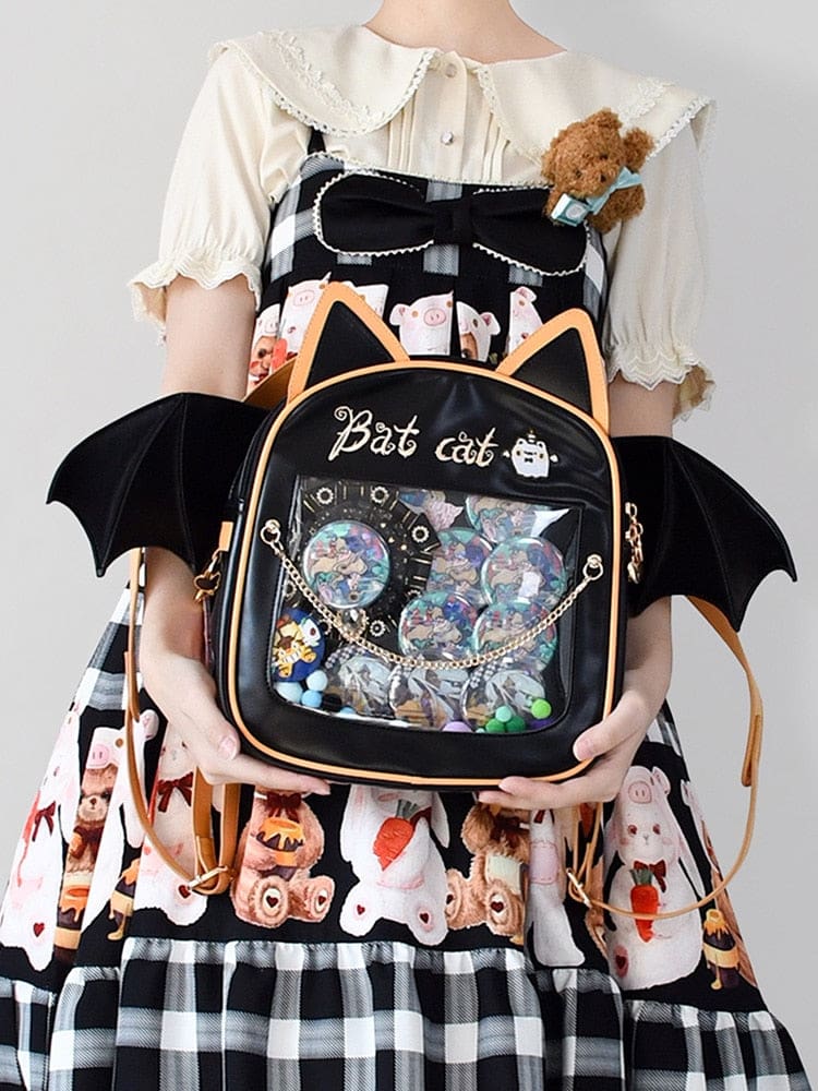 Bat cat backpack worn with a collared blouse and Halloween-print outfit, showing a collection of badges through the transparent front pocket.