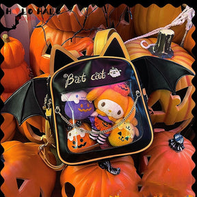 Black Bat cat display backpack arranged among pumpkins, with orange and purple plushies behind the clear pocket and a draped gold-tone chain across it.