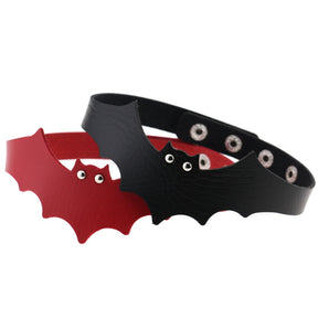 Black and red bat wing chokers overlap on a white background. The scalloped wings, pointed ears, eyelet eyes and rows of snap fasteners are visible.