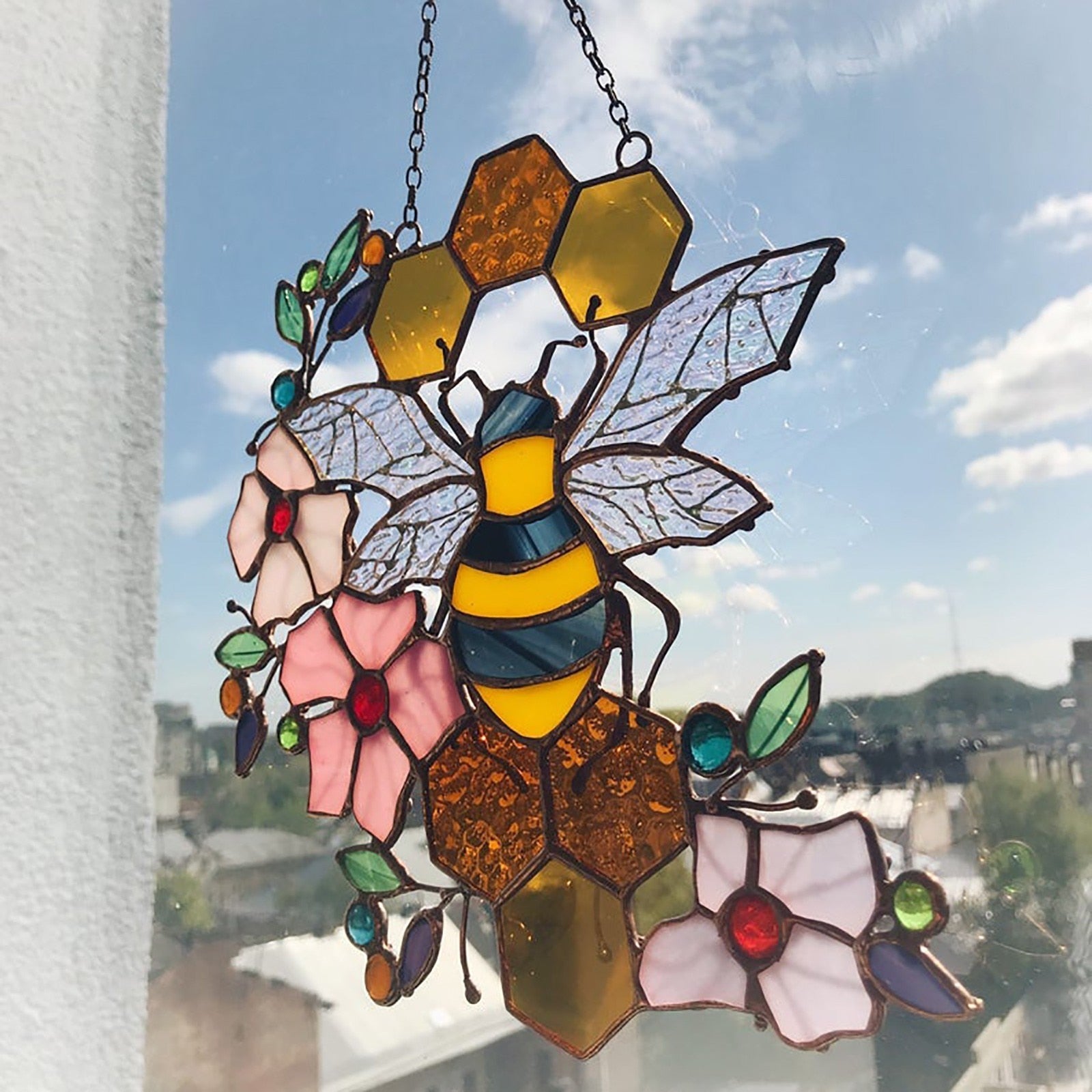 Bee and honeycomb stained glass hanging displayed at a window against blue sky.