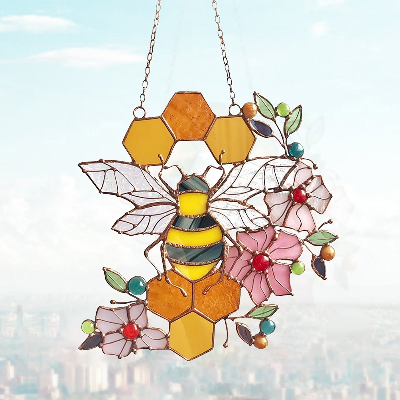 Bee and honeycomb stained glass hanging displayed against a city window view.