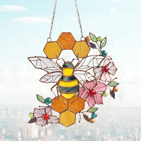 Bee and honeycomb stained glass hanging displayed against a city window view.