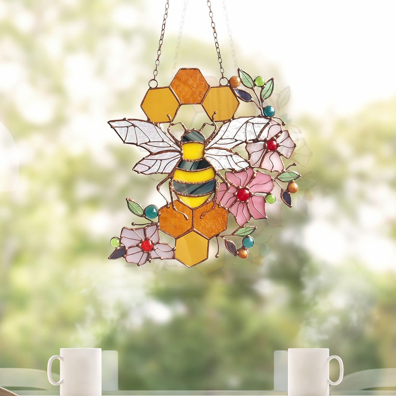 Bee and honeycomb stained glass hanging shown above cups on a window ledge.