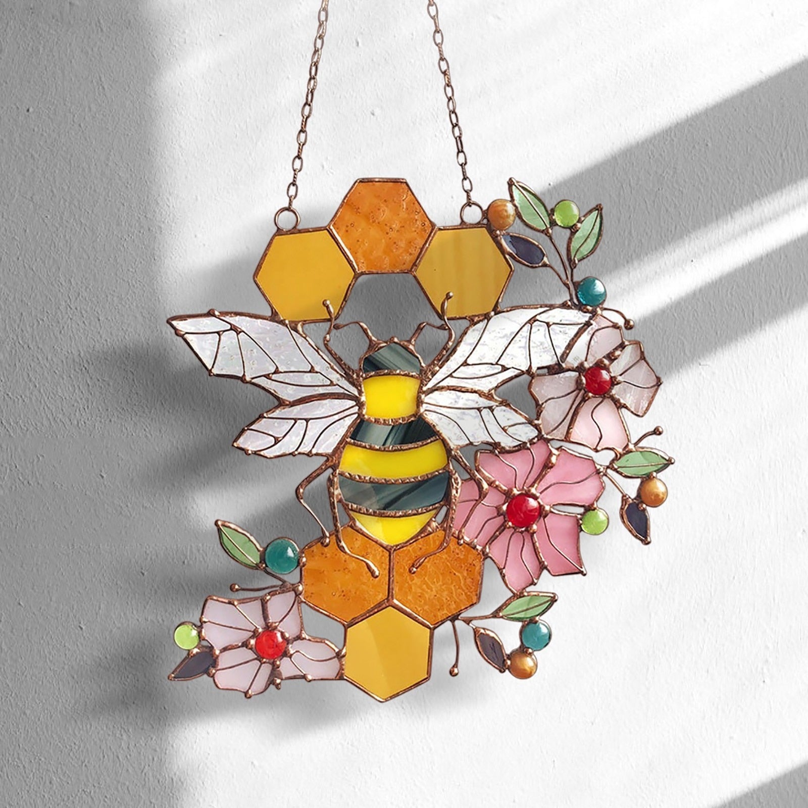 Bee and honeycomb stained glass hanging displayed on a wall in sunlight.