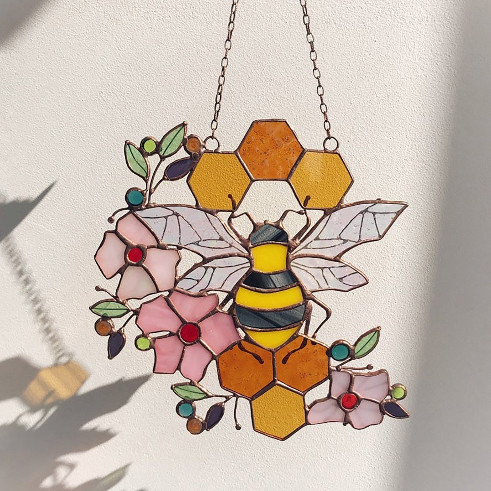 Bee and honeycomb stained glass hanging shown with a bee-shaped shadow on a light wall.
