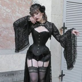 Portrait crop of the black lace bell-sleeve overlay styled with a separate corset and lace stockings against an old stone building.