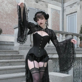 Black floral lace overlay worn over a corset, with one arm lifted beside pale stone stairs and an ornate railing.